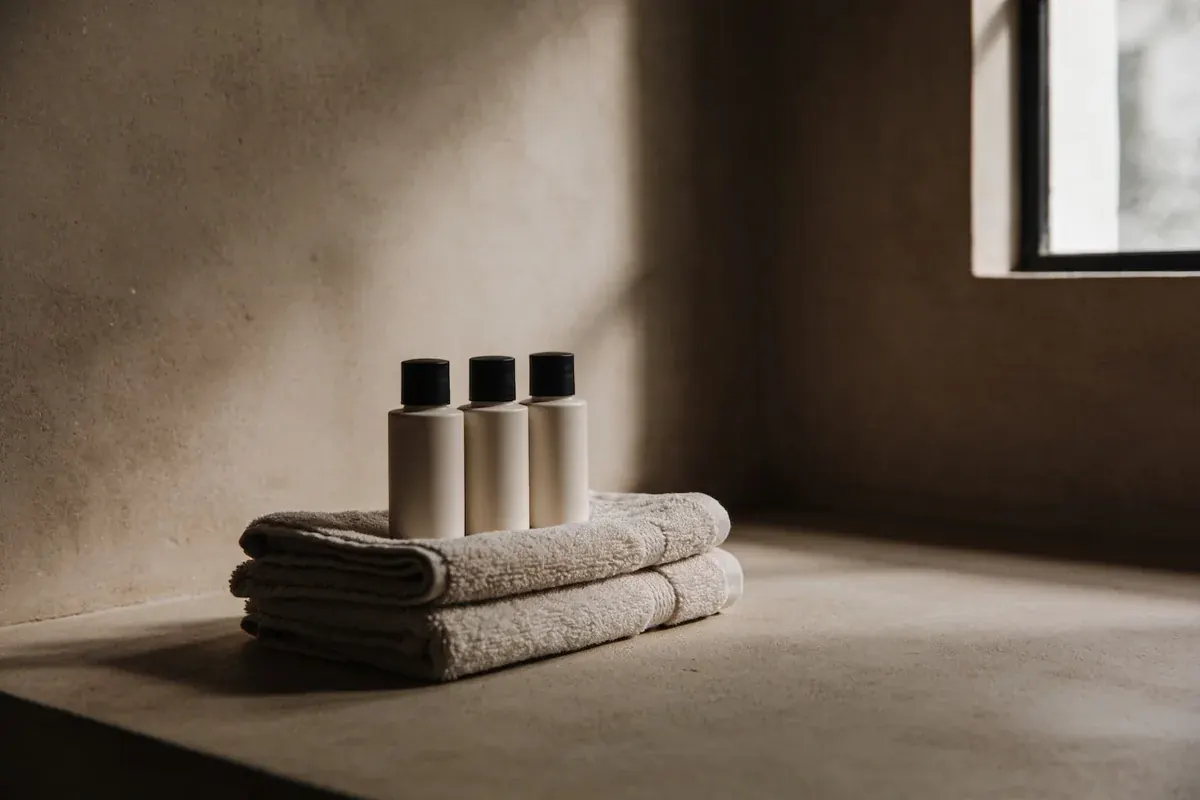 A small set of unlabeled travel-sized bottles resting on a folded towel in soft light, travel skincare essentials